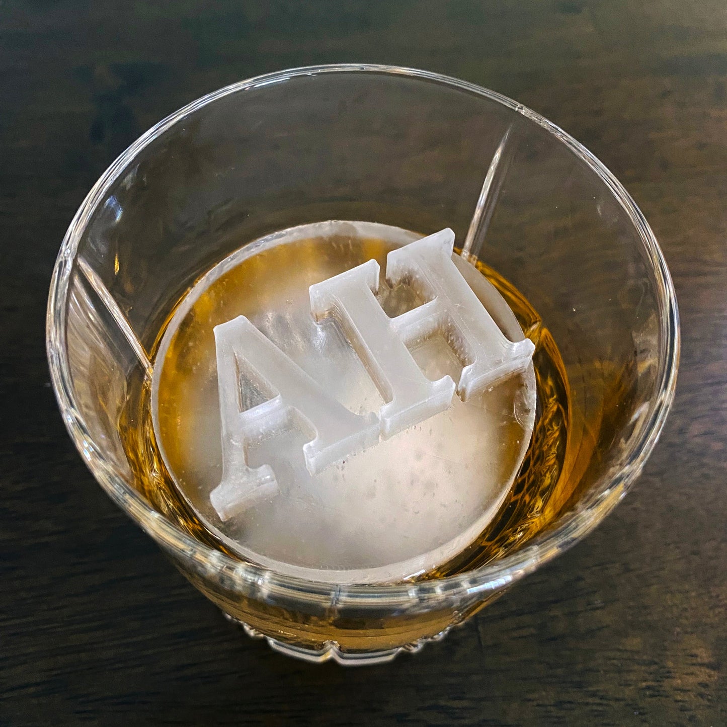 Ice cube with 'ALP' letters in a glass of alcohol on a dark surface
