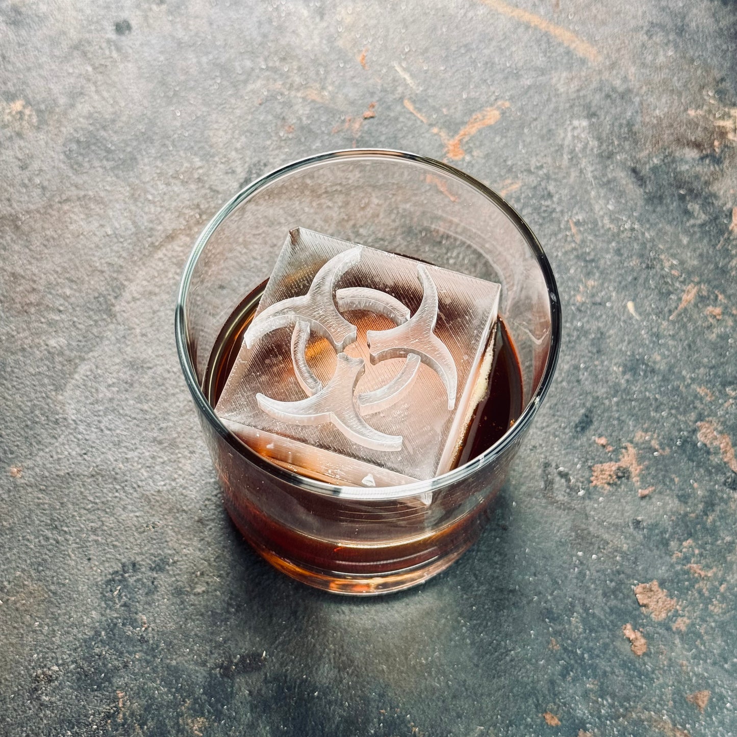 Clear ice cube with biohazard emblem in whiskey glass