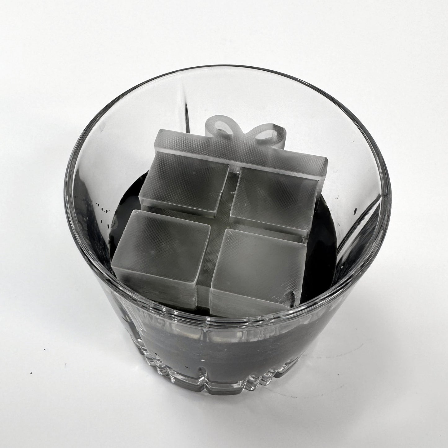 A clear glass ice mold with a Christmas present shape, containing water and ice.