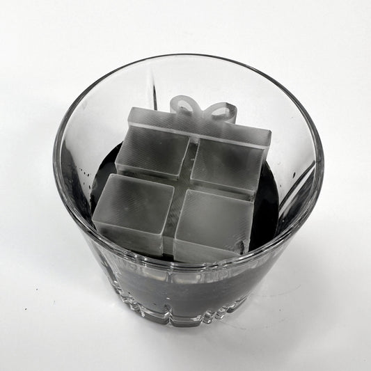 A clear glass ice mold with a Christmas present shape, containing water and ice.