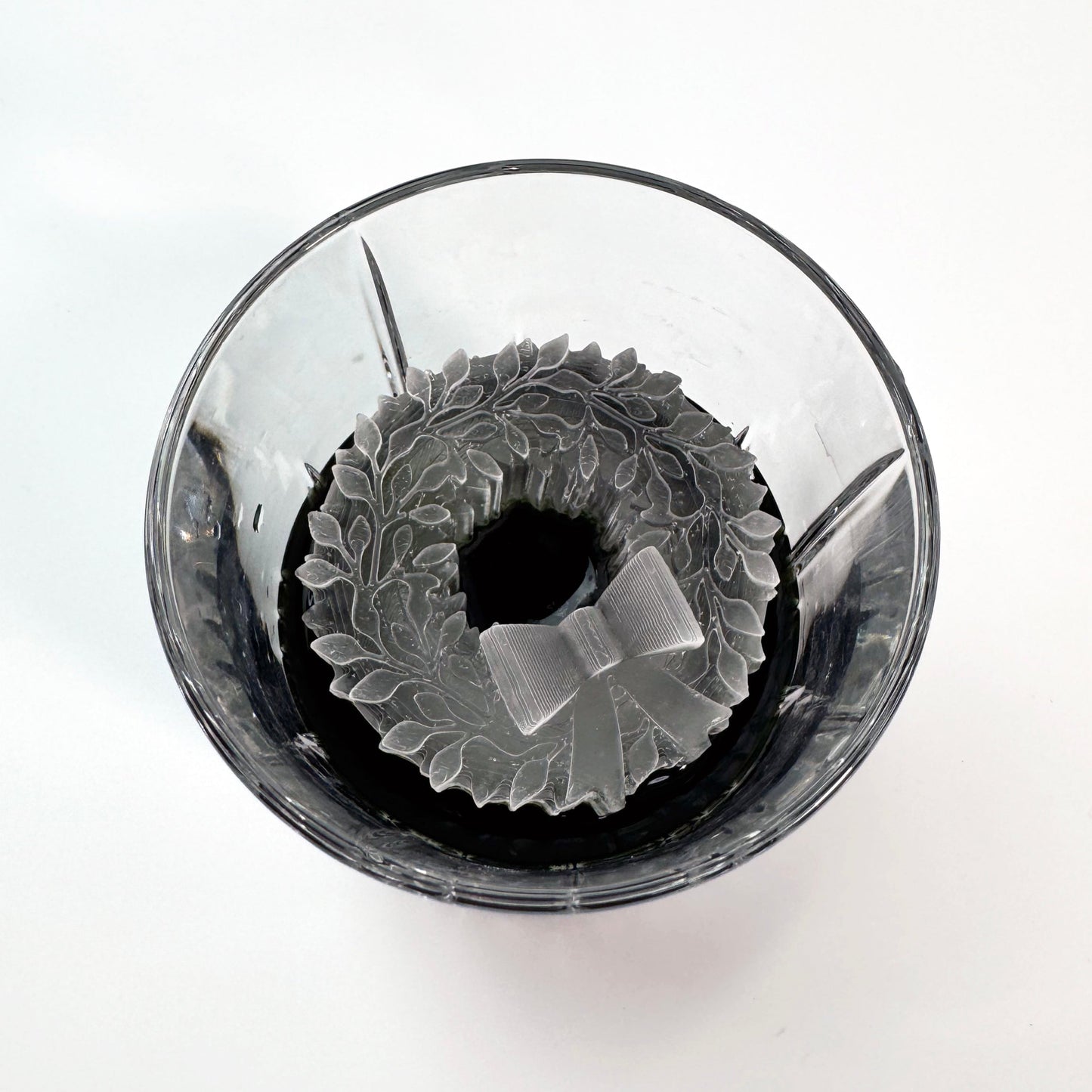 A clear glass ice mold with a Christmas wreath design, containing frozen ice.