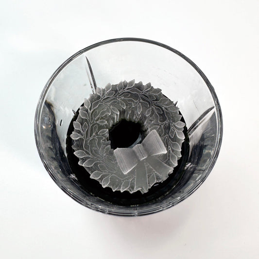 A clear glass ice mold with a Christmas wreath design, containing frozen ice.