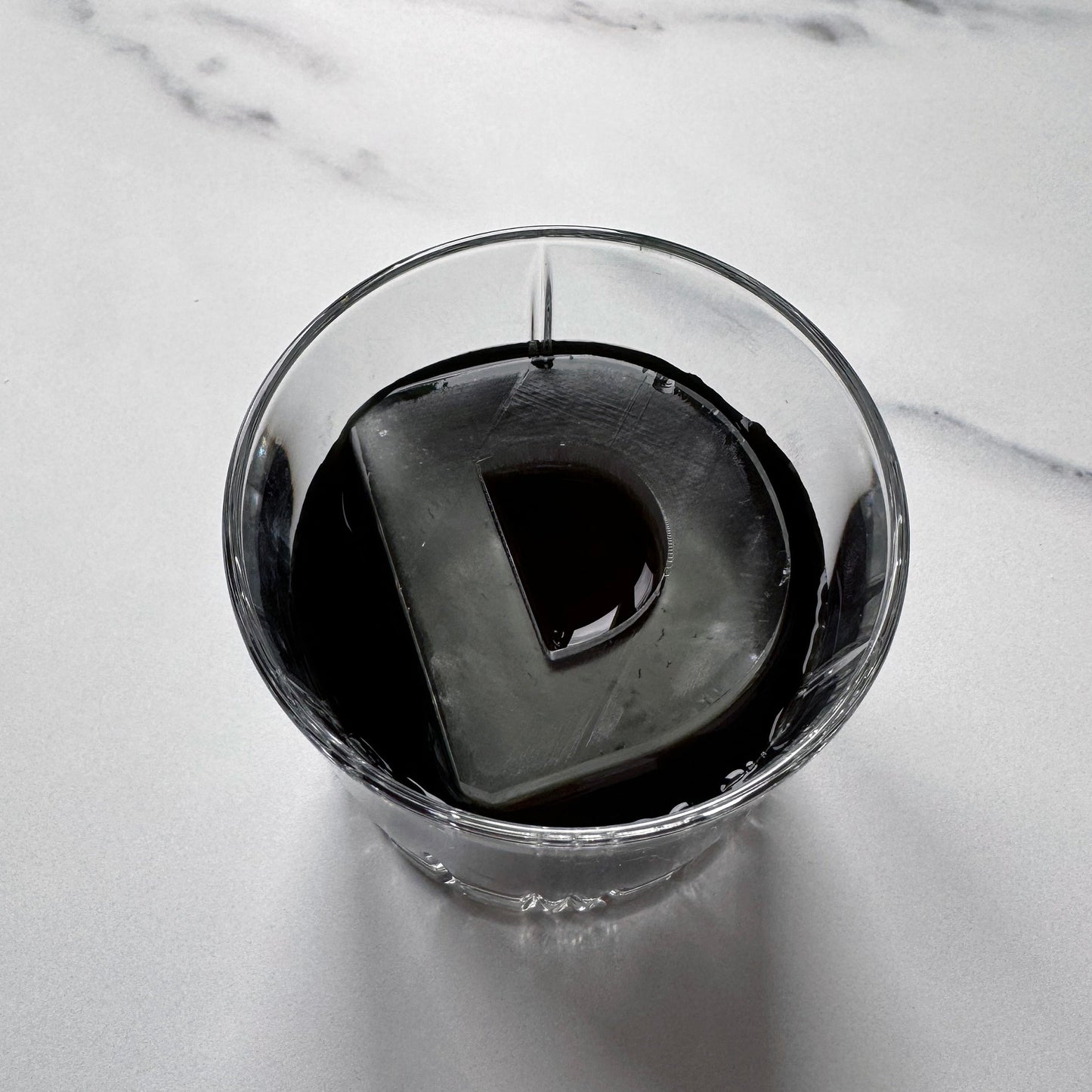 An ice tray with a silicone mold in the shape of the letter 'D', with water filling the tray, set on a white background.
