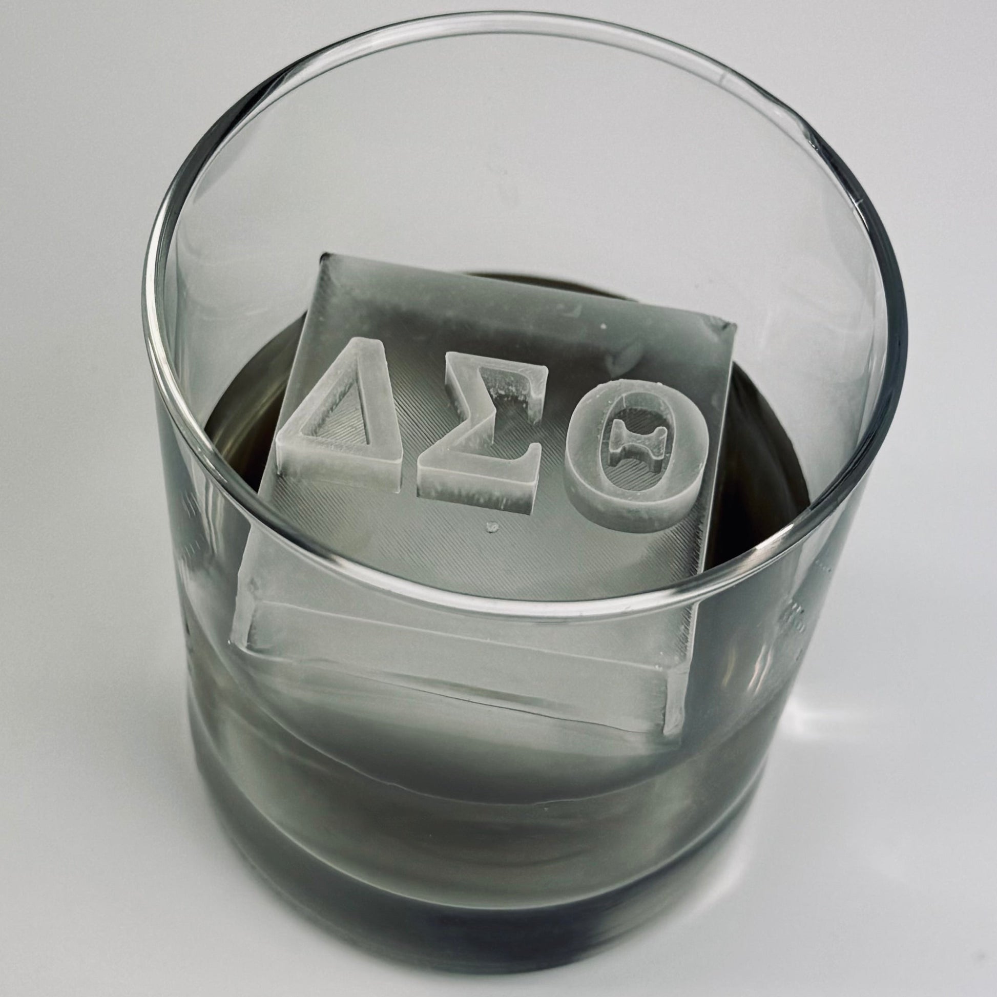 Clear glass with ice cubes featuring Greek letters on a gray background
