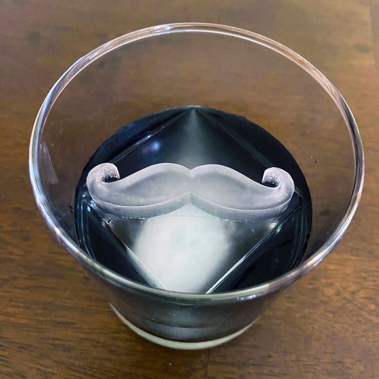 A glass with a solid white mustache-shaped ice cube inside it.