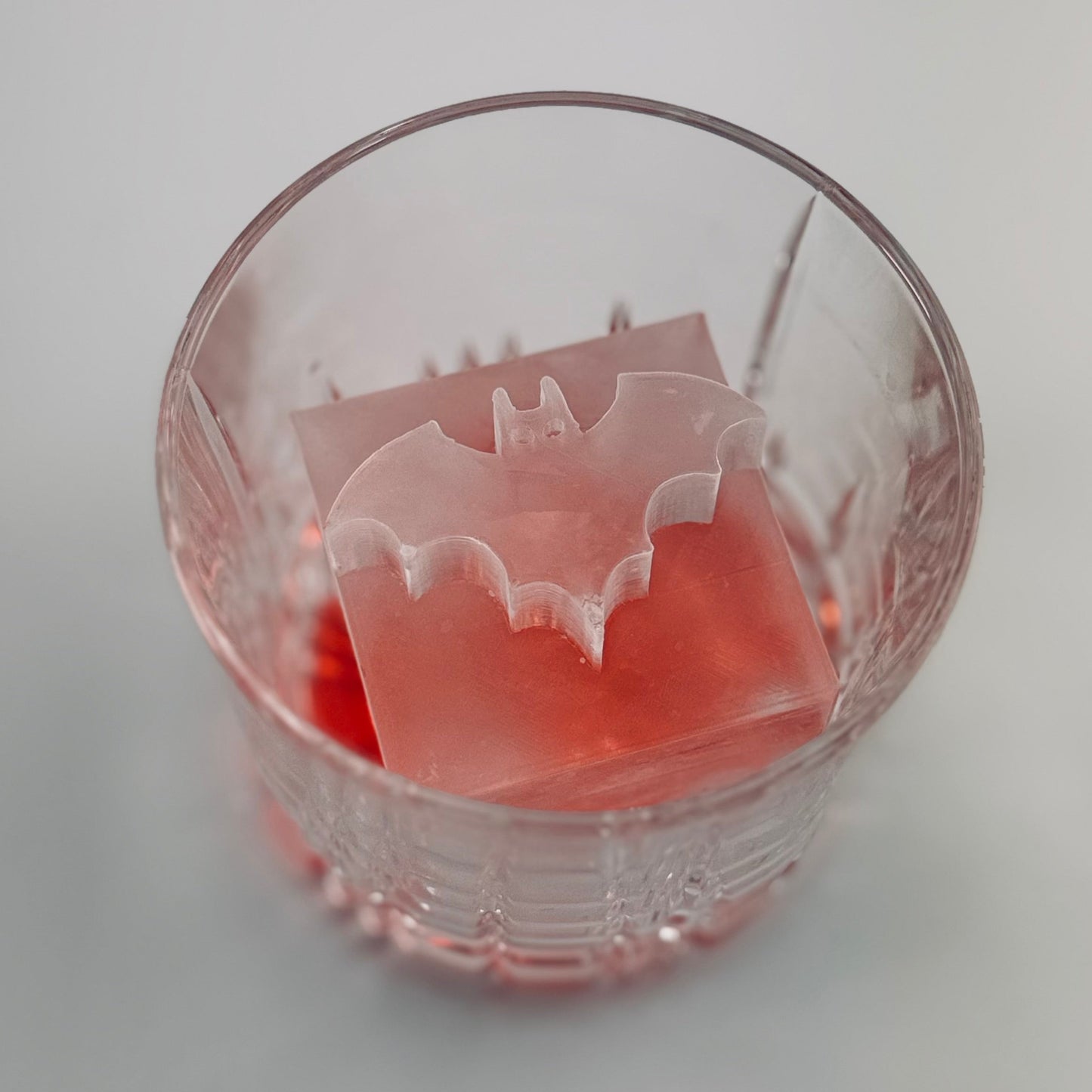 Clear glass with a red liquid and a Batman ice cube on a white background
