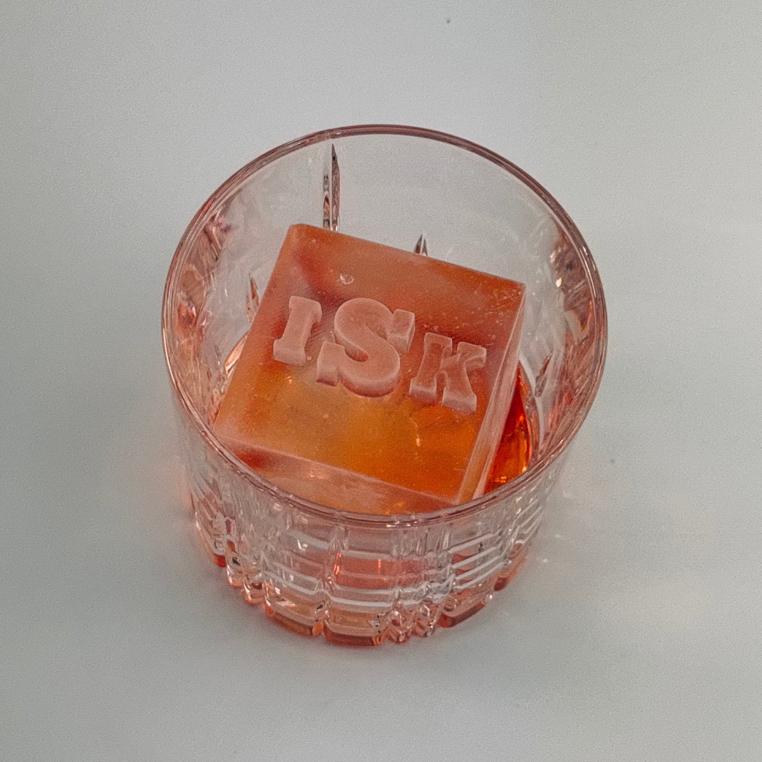 Square orange ice with 'ISK' branding in a clear glass container on a white background