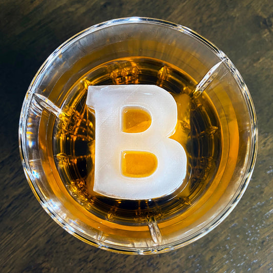 A letter 'B' shaped ice mold placed inside a cocktail glass filled with a brown liquid.