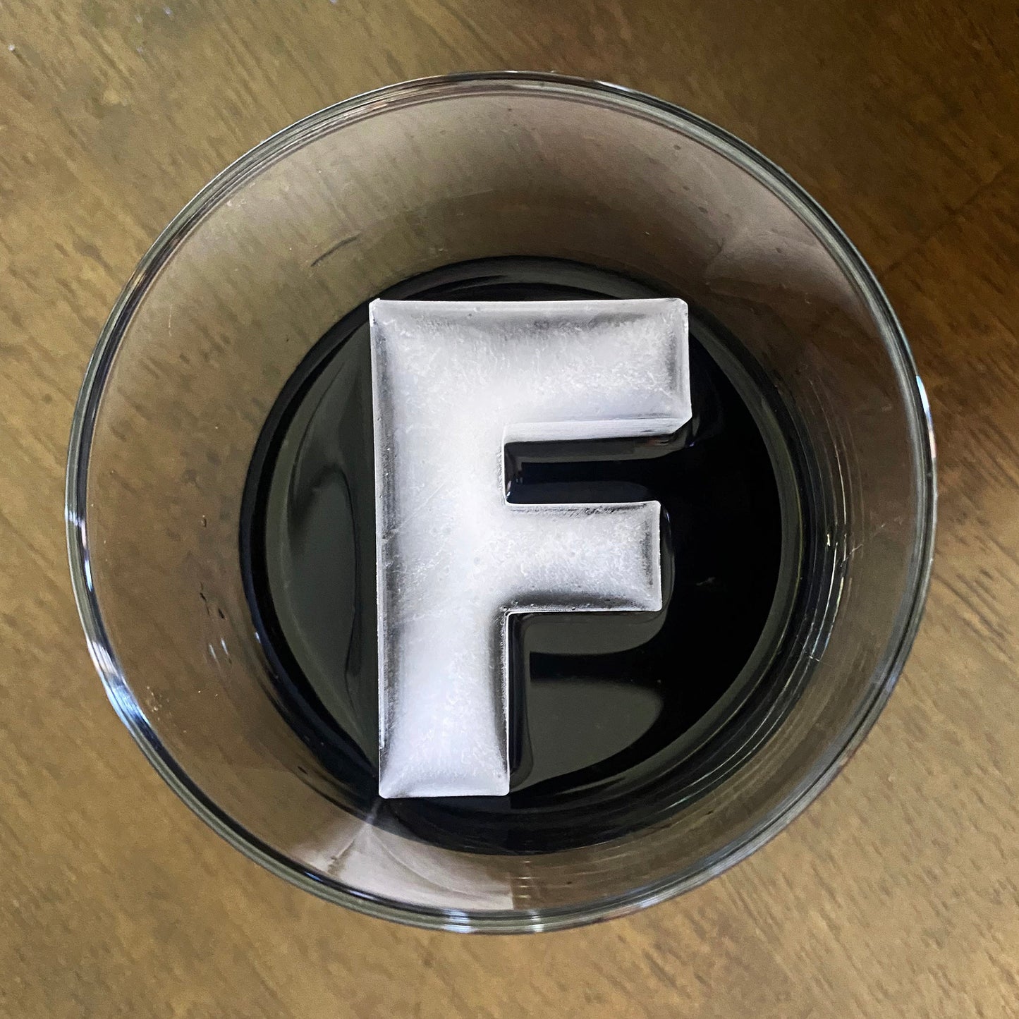 A letter-shaped ice mold tray filled with ice in the shape of the letter 'F', placed inside a cocktail glass.
