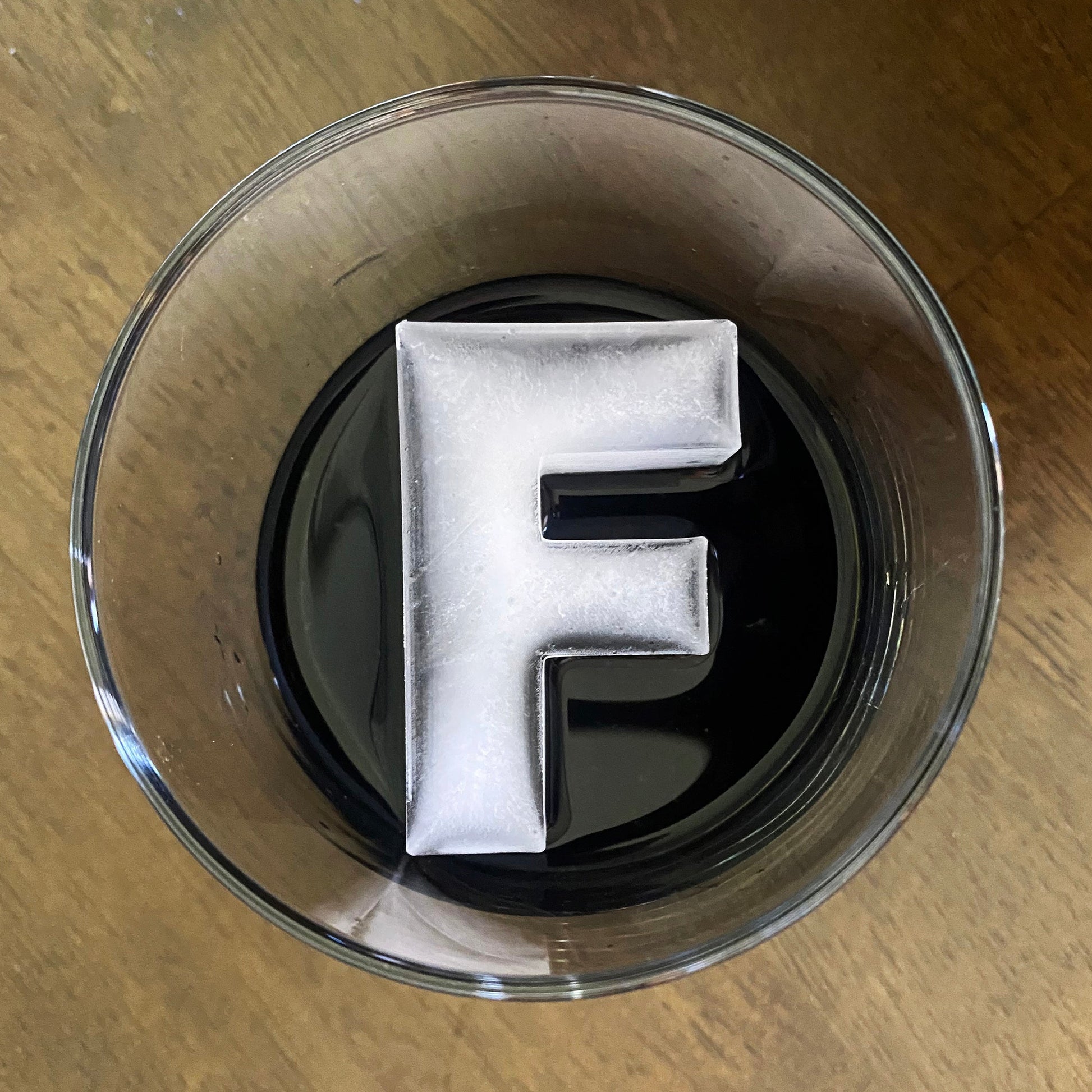 A letter-shaped ice mold tray filled with ice in the shape of the letter 'F', placed inside a cocktail glass.