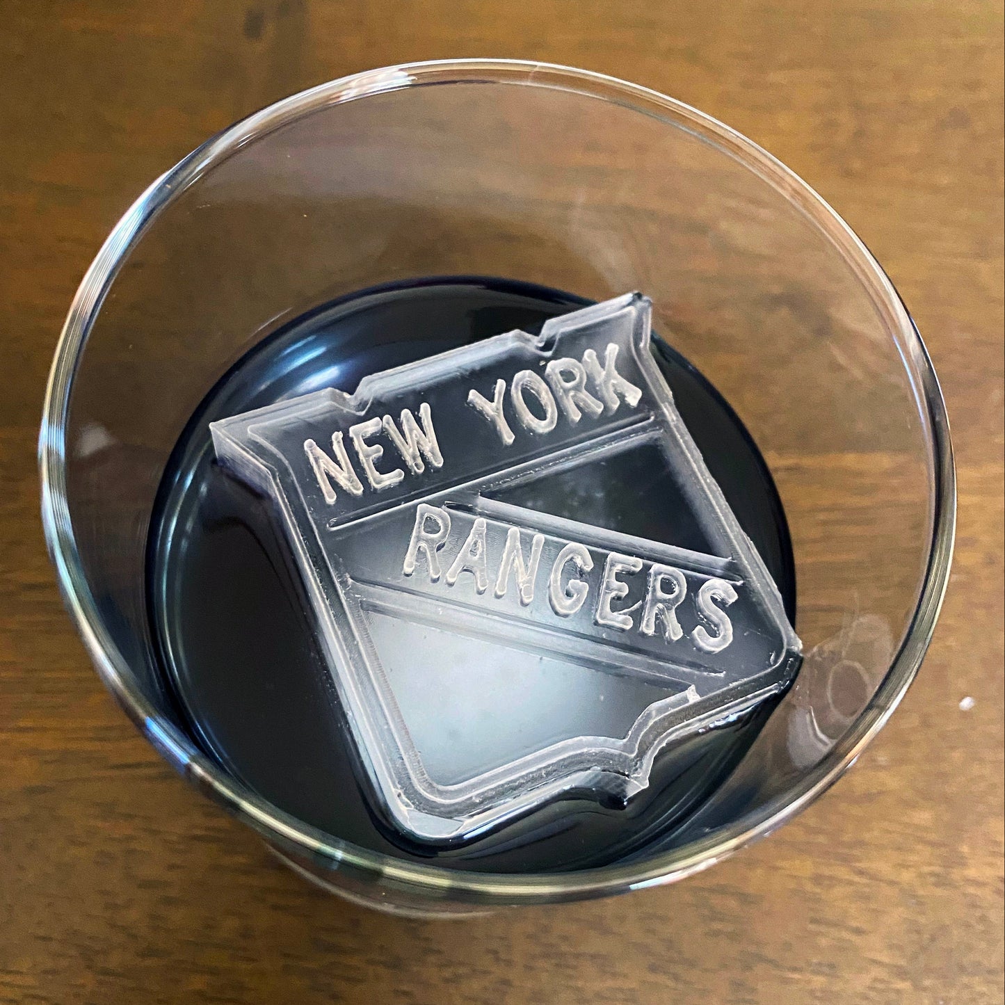 A clear ice mold with the text 'NEW YORK RANGERS' on it, placed inside a glass.