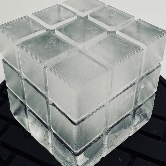 A clear silicone ice cube mold designed to resemble a Rubik's cube, placed on a black surface.
