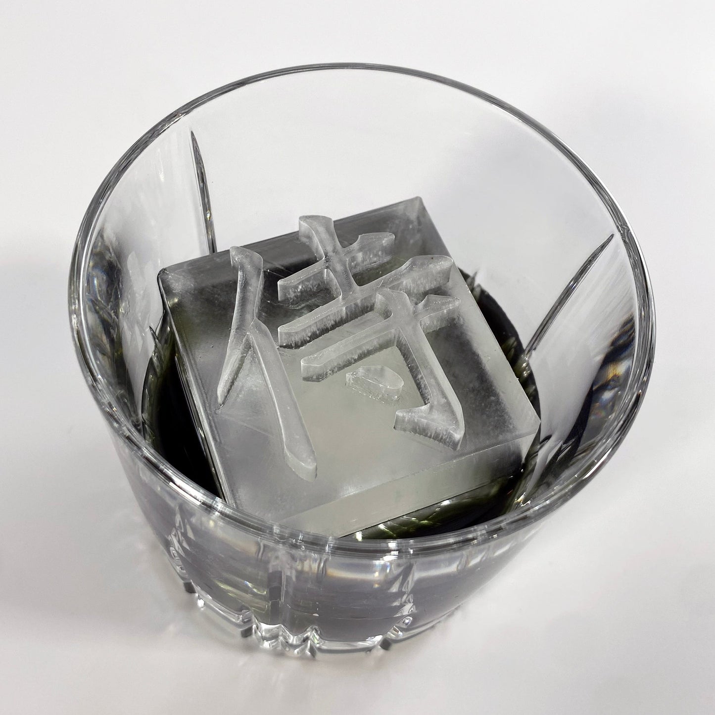 A clear ice mold with the Japanese character for 'Samurai' printed on the surface, placed inside a glass.