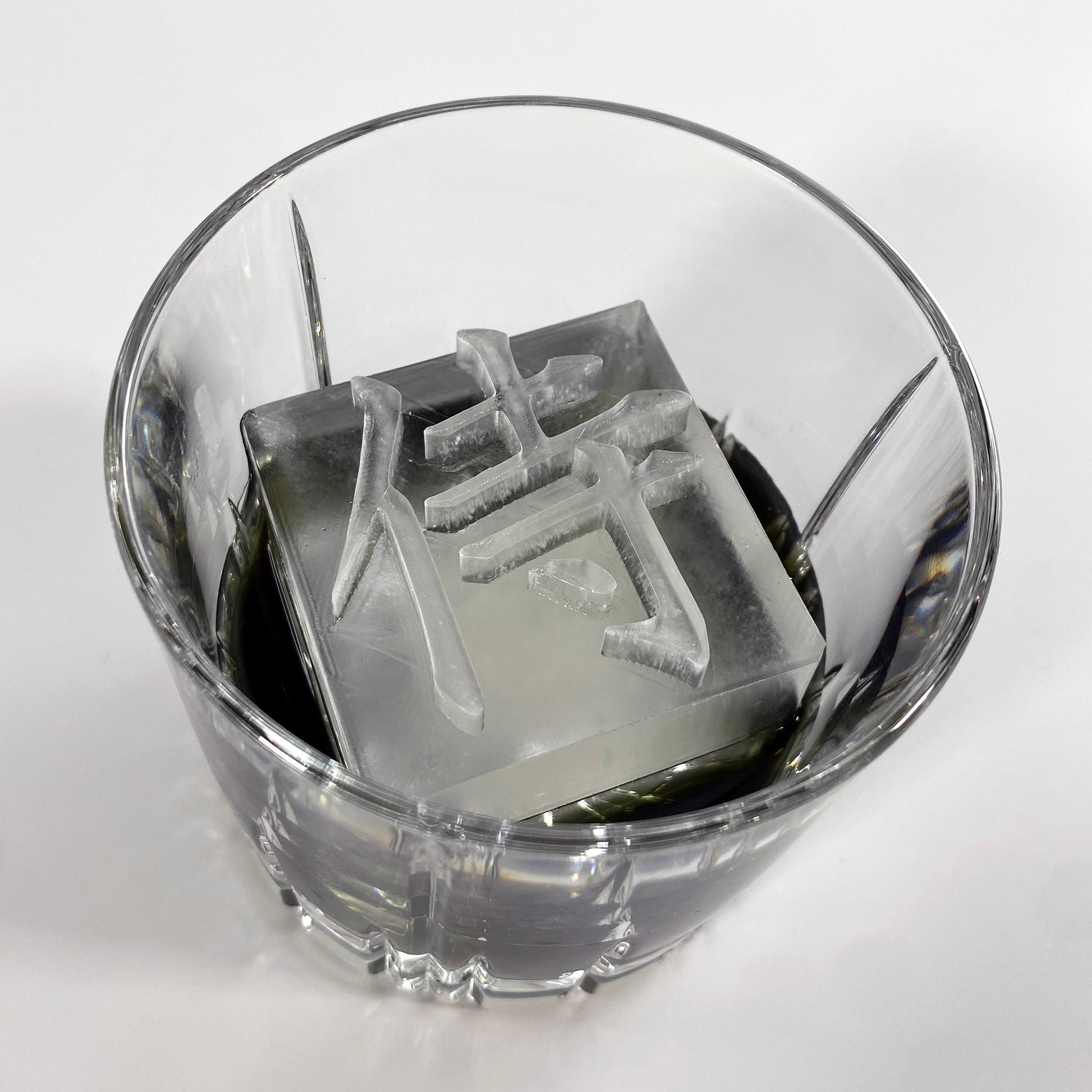 A clear ice mold with the Japanese character for 'Samurai' printed on the surface, placed inside a glass.