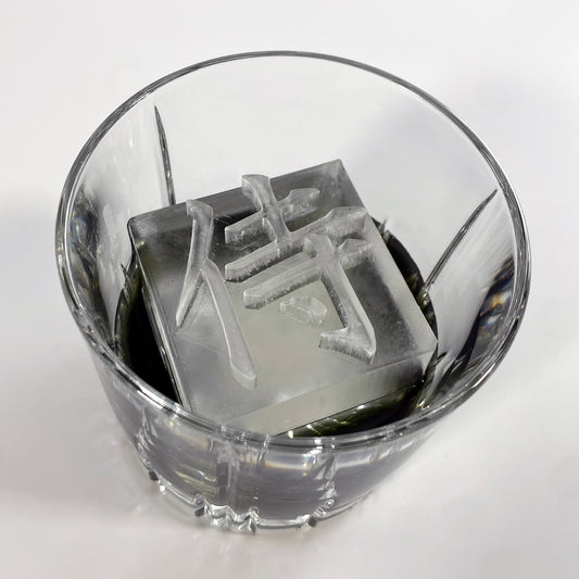 A clear ice mold with the Japanese character for 'Samurai' printed on the surface, placed inside a glass.