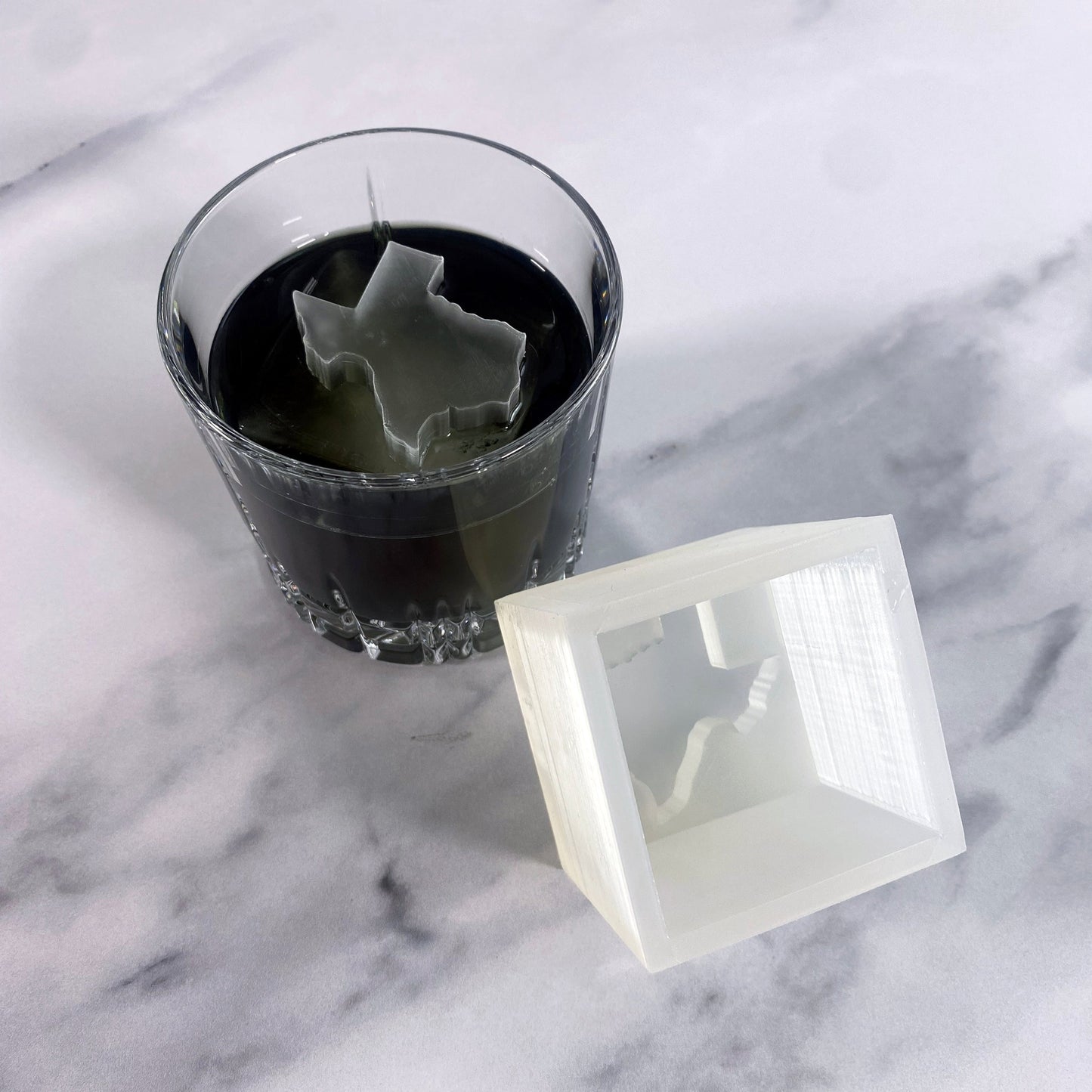 Texas Ice cube in a glass of dark liquid on a marble surface