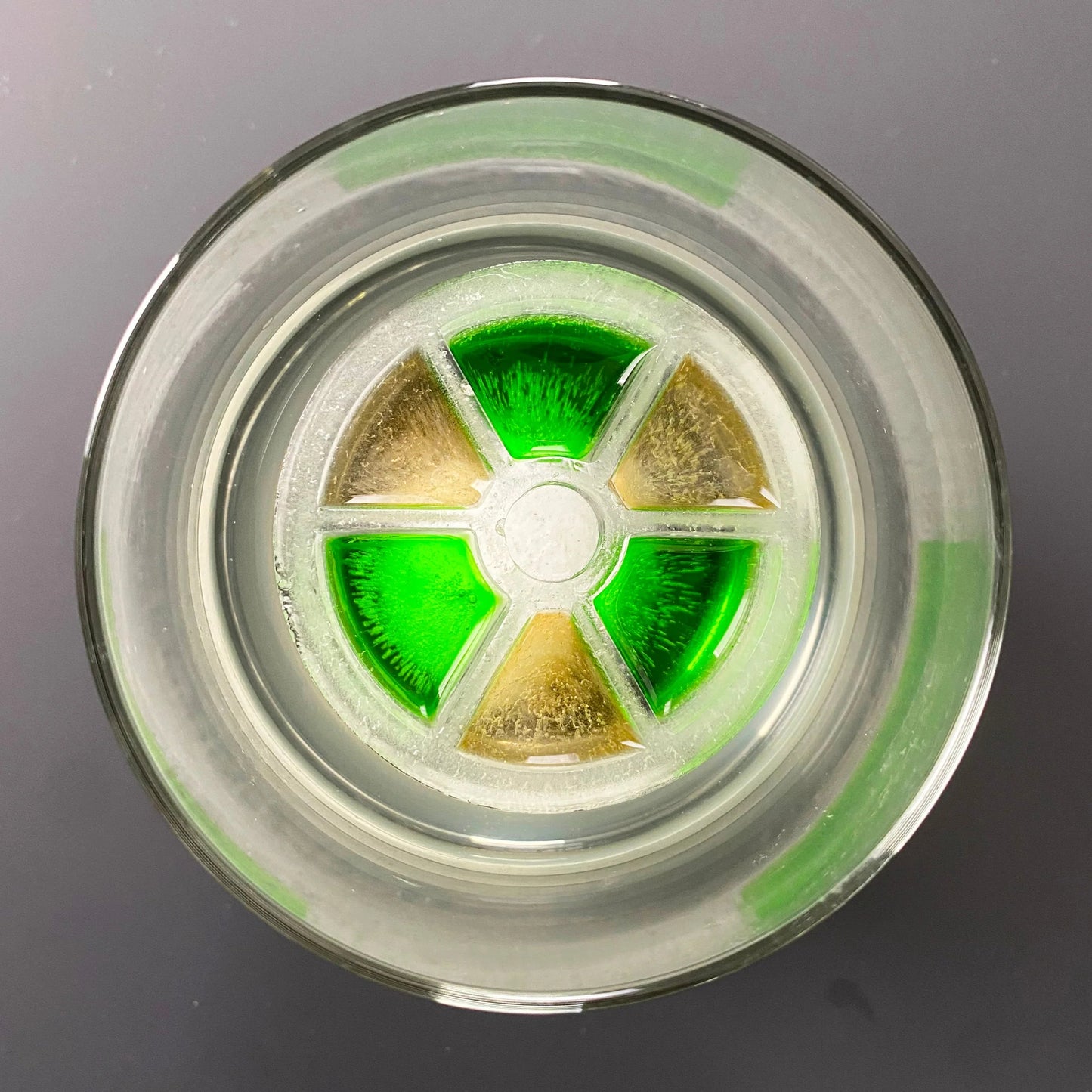A green and clear silicone ice mold with a biohazard design, placed inside a glass.