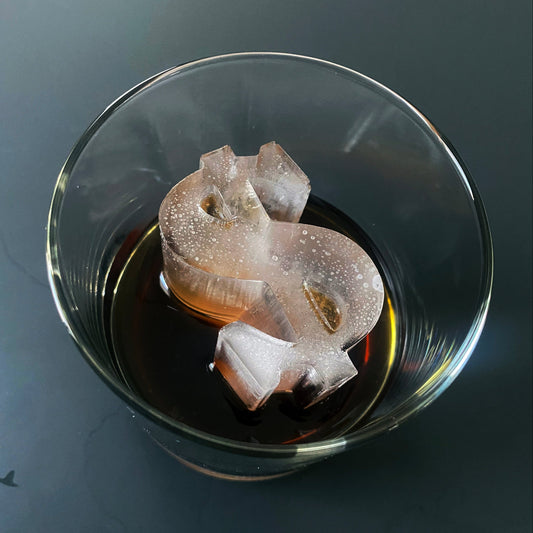 A clear glass ice mold in the shape of a dollar sign, partially filled with a dark liquid, likely to be used for creating ice sculptures.