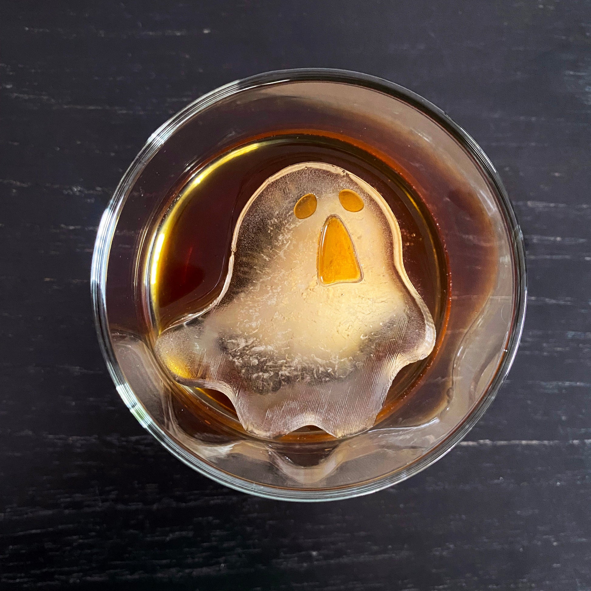 A clear ice mold in the shape of a ghost placed in a glass filled with liquid, likely to be a Halloween-themed drink.