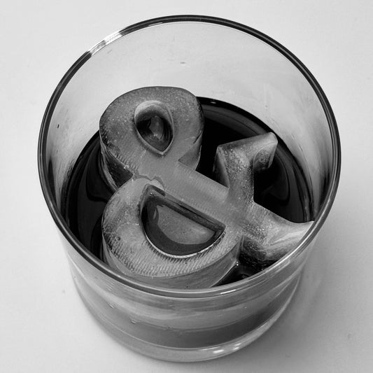 Glass with an ice cube shaped like an ampersand on a white background