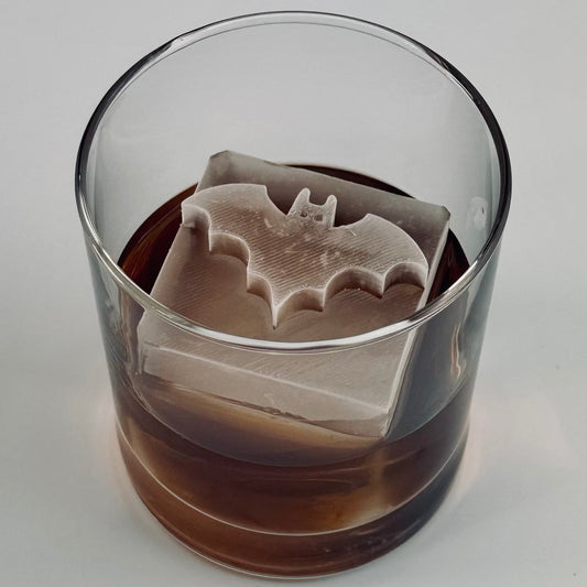 Glass with a bat-shaped ice cube and dark liquid on a light gray background