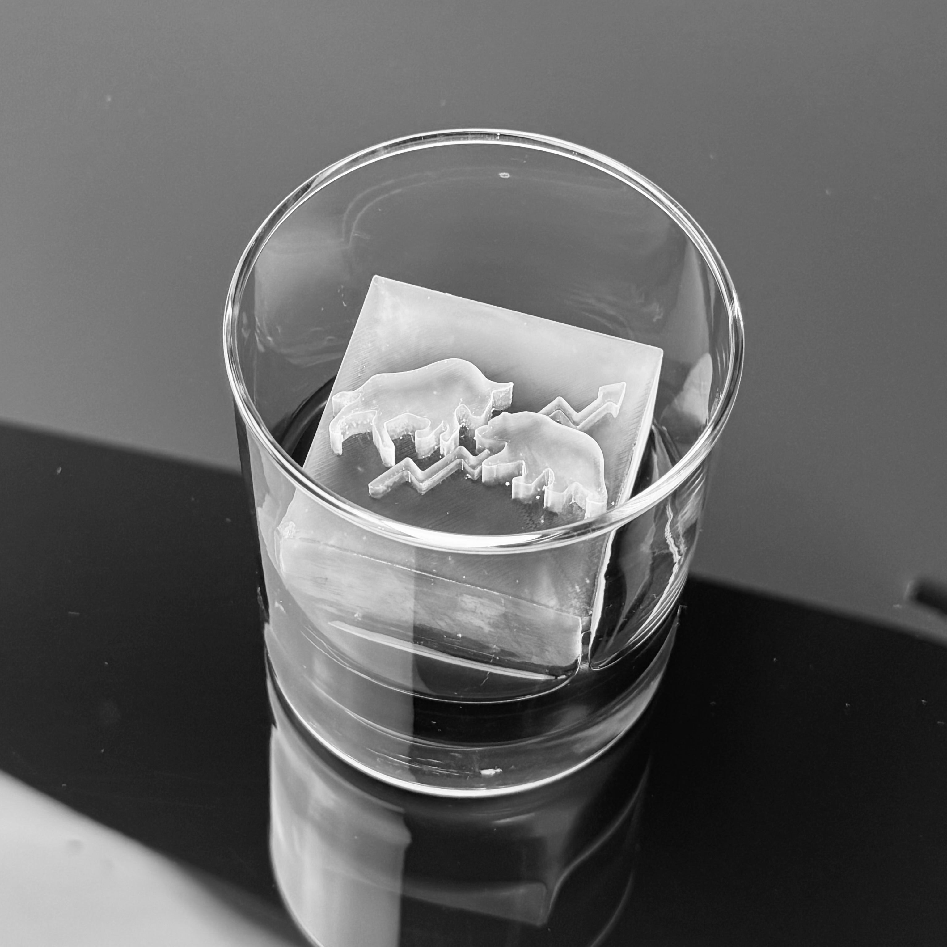 Clear glass with a ice cube featuring a bull and bear symbol on a black countertop