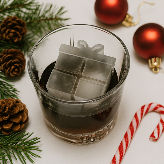 Glass of dark liquid with ice cubes, surrounded by Christmas decorations on a white surface.