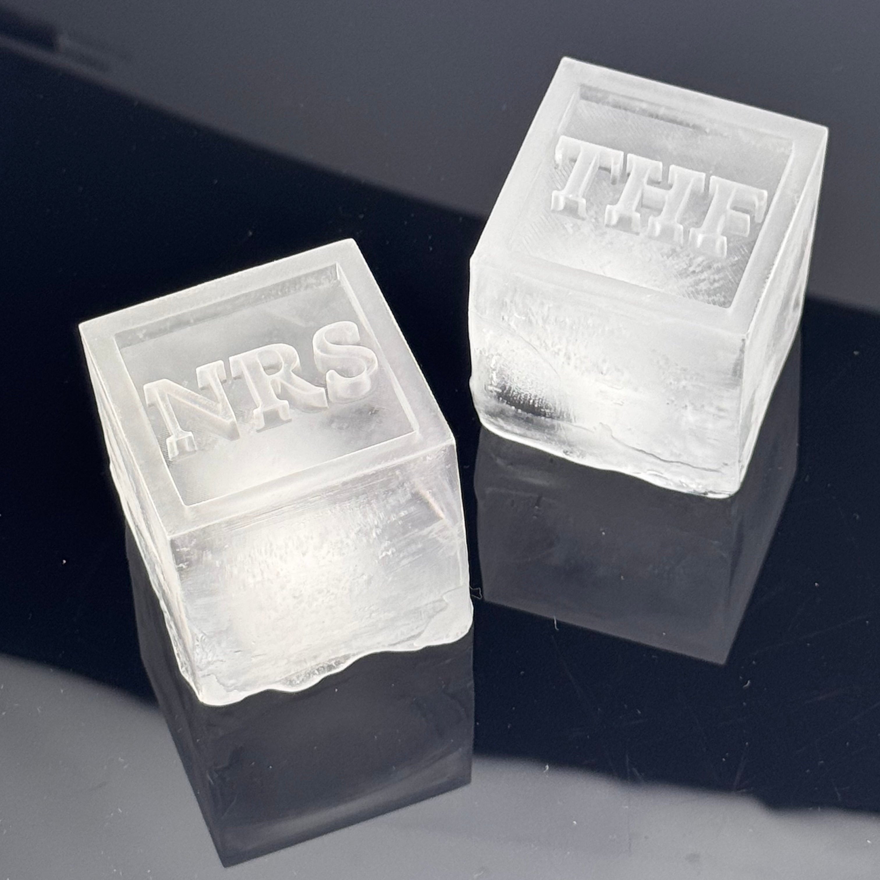 Two clear ice cubes with 'NRS' and 'THF' embossed on them against a dark background.