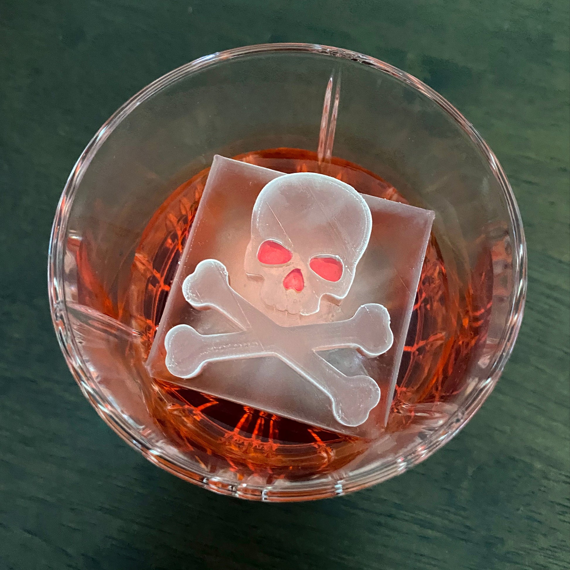 Clear glass with a skull and crossbones ice cube on a dark surface
