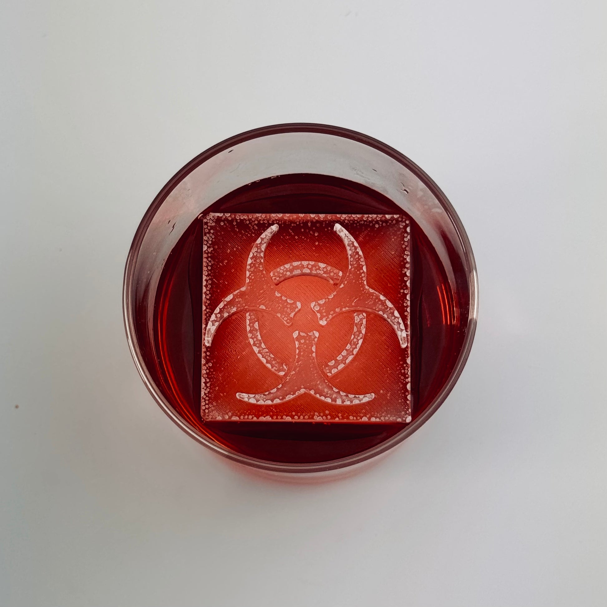 Glass of red liquid with a biohazard symbol ice cube on a white background