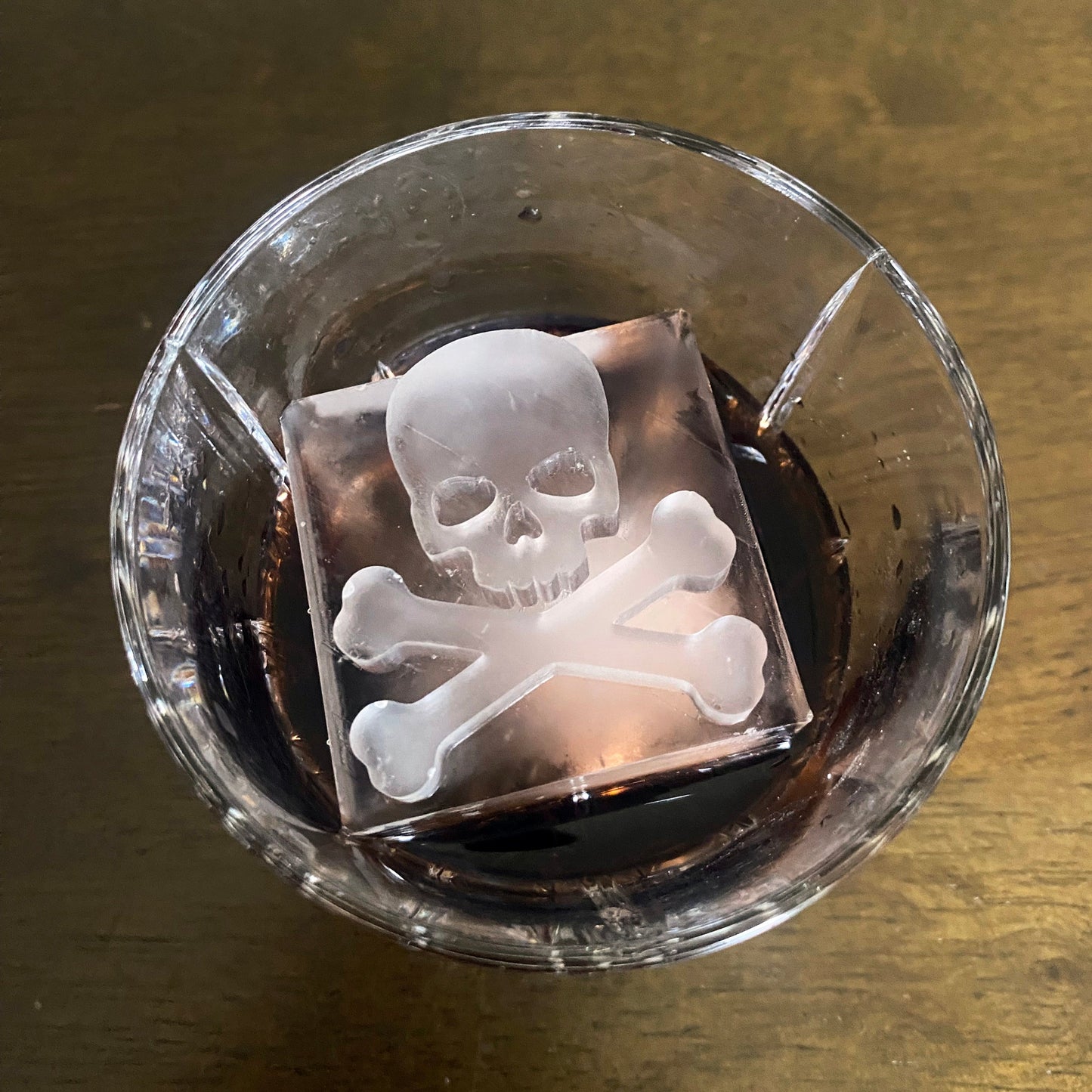 Clear glass with a skull and crossbones ice cube on a wooden surface
