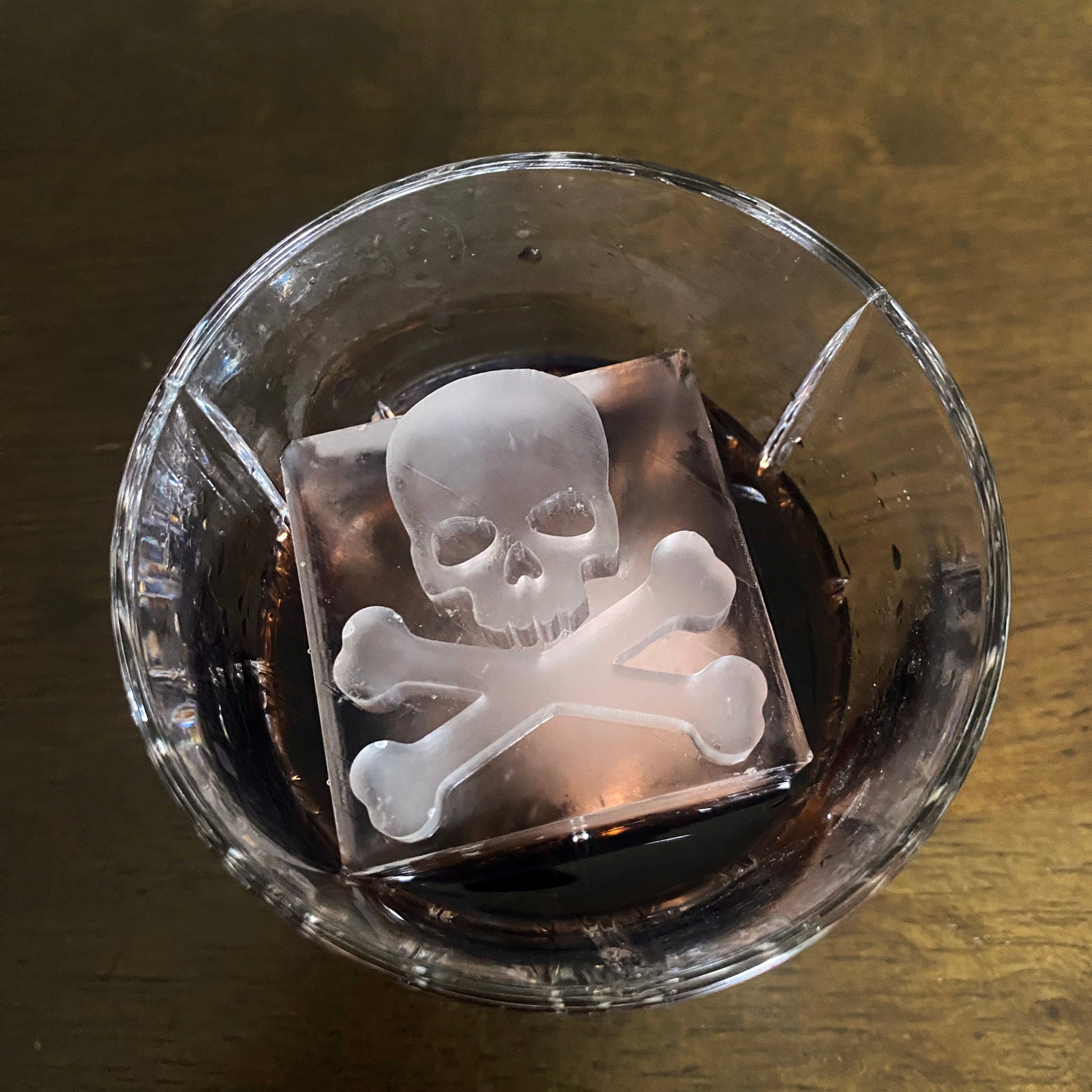 Clear glass with a skull and crossbones ice cube on a wooden surface
